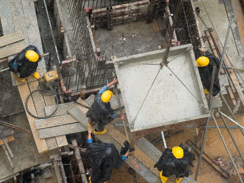 Construction workers in yellow hard hats removing an item from a crane in bad weather 